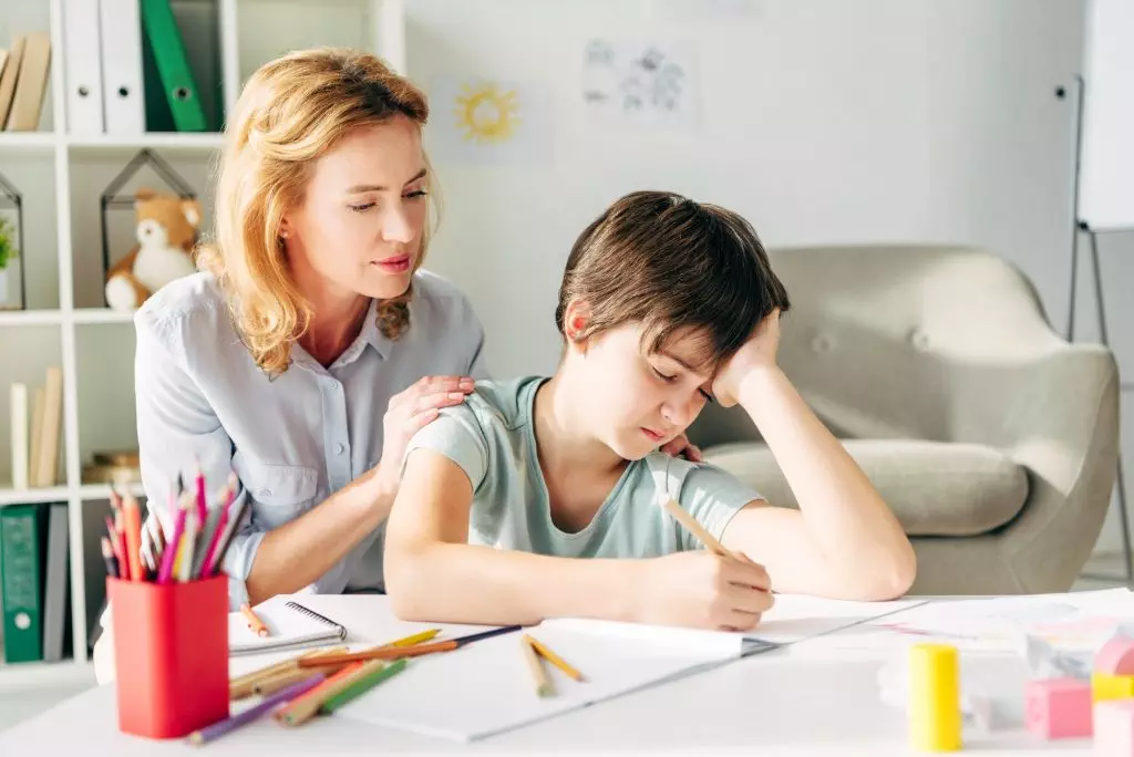 kid with dyslexia drawing with pencil and child psychologist looking at it