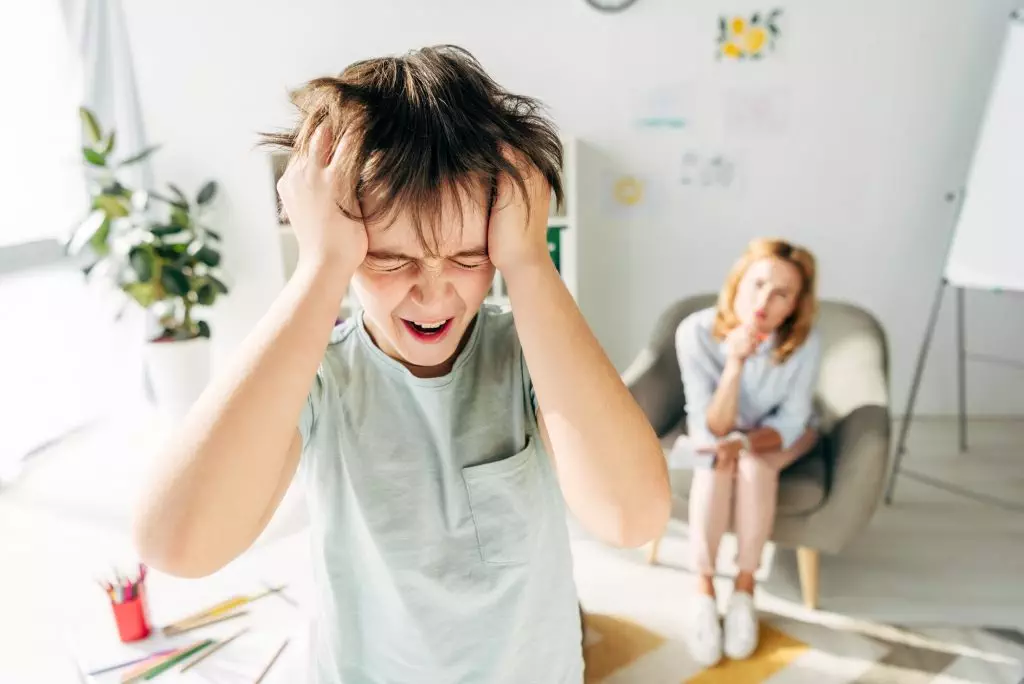 selective focus of irritated kid with dyslexia shouting and holding head